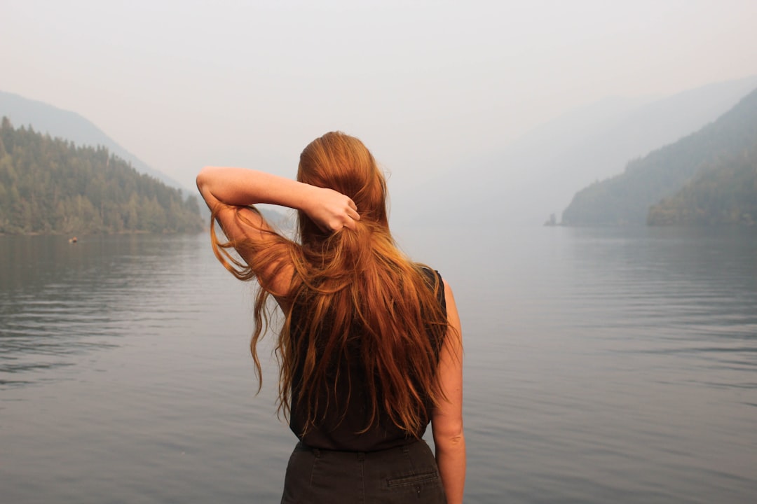Photo by KaLisa Veer woman holding hair facing body of water during daytime